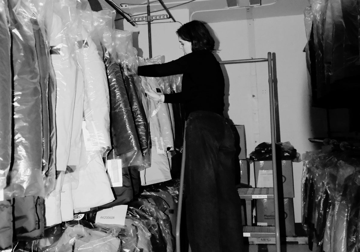 Photo en noir et blanc d'une femme cherchant un manteau Audvik sur un des portants de l'atelier.