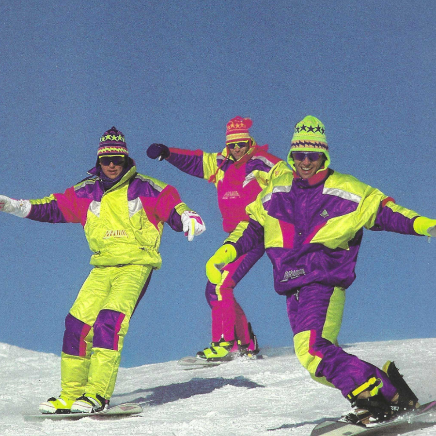 Trois hommes portant des tenues vintage Audvik et descendant une montagne en snowboard.