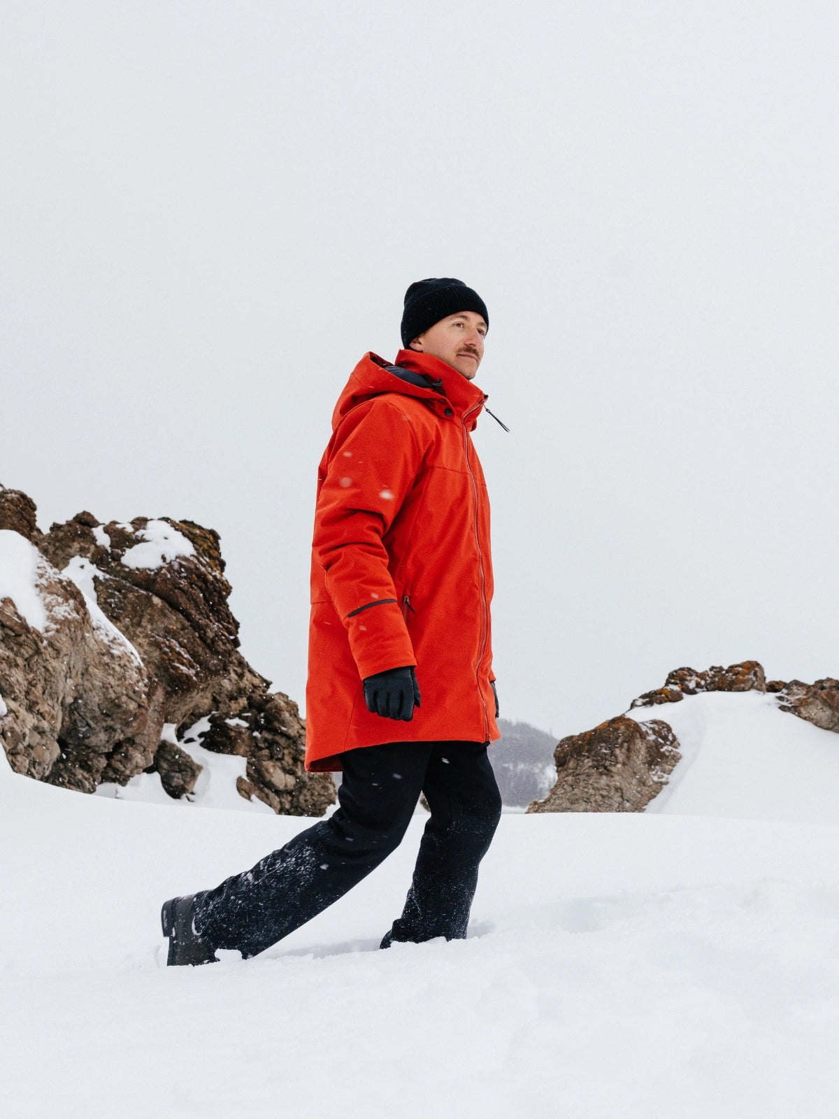 Homme dans un paysage hivernal rocheux portant un manteau d'hiver pour homme rouge et une tuque noire. 