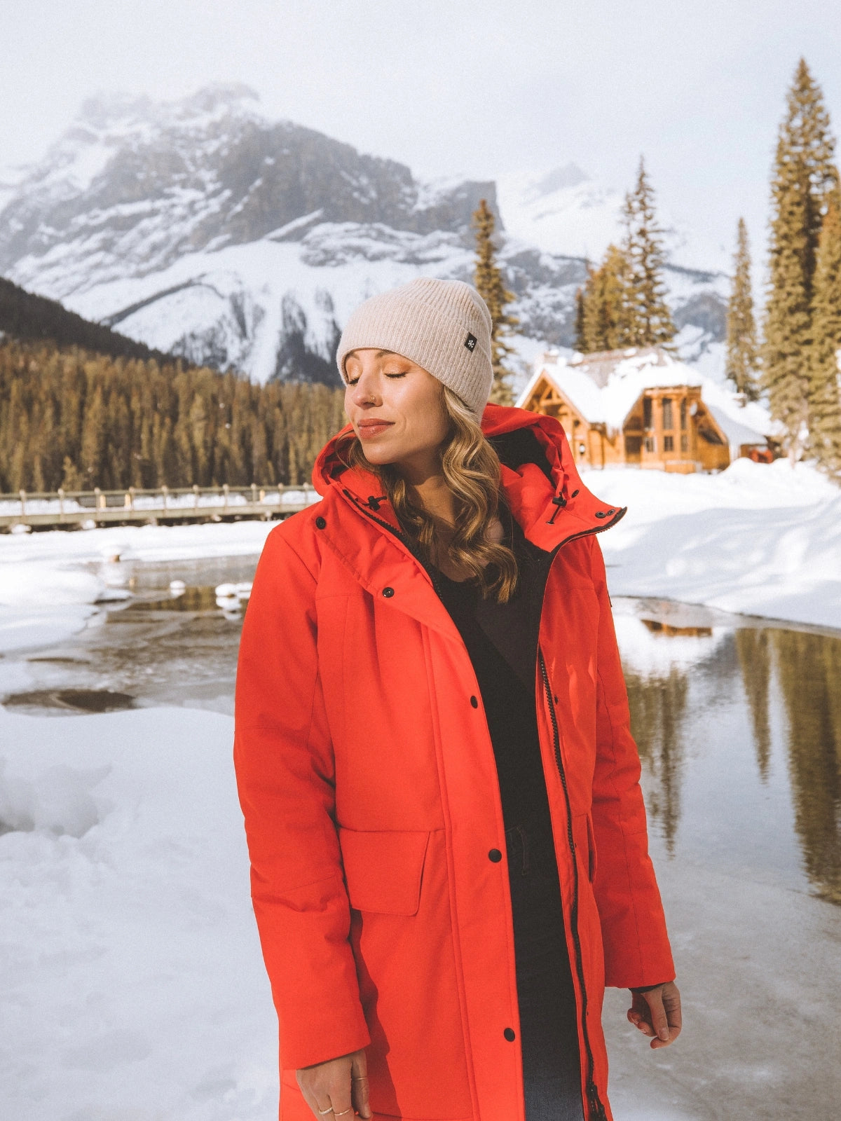 Femme dans un paysage hivernal portant un bonnet beige en cachemire et un manteau d'hiver rouge Audvik.