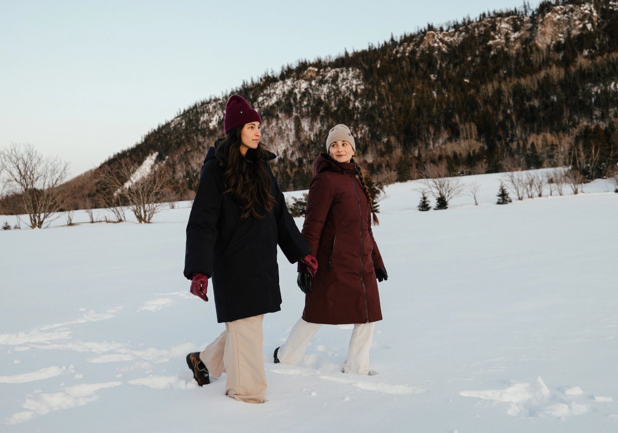 Deux femmes marchant dans la neige portant des manteaux longs de la nouvelle collection Audvik ainsi que des tuques en cachemire Audvik. 